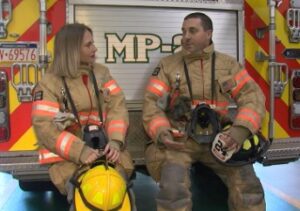 Two firefighters talk to each other while sitting on a fire truck.