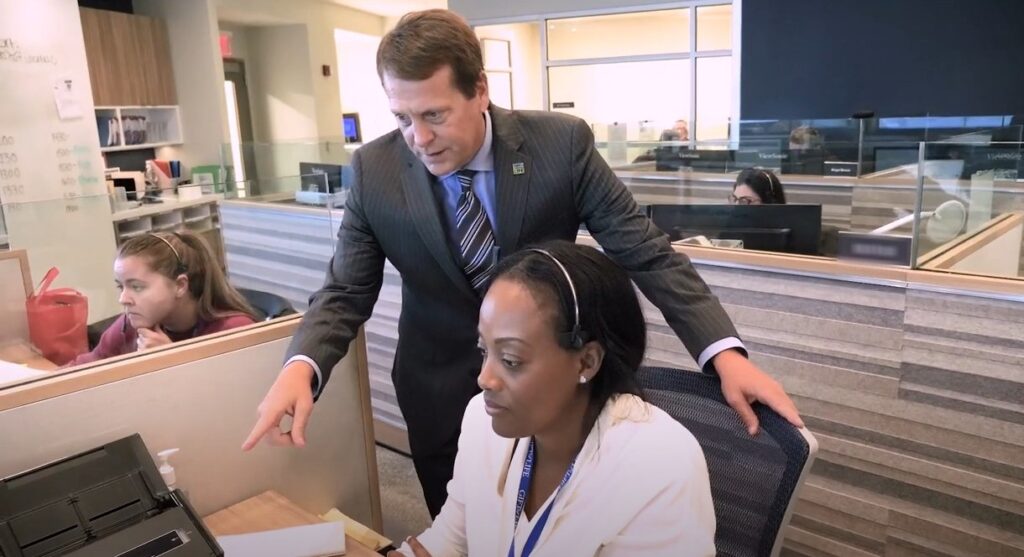 A man stand over a desk as a woman works on the computer.