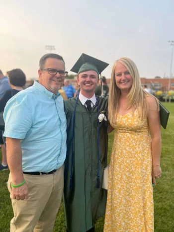 A high school graduate poses for a photo with his mother and father.