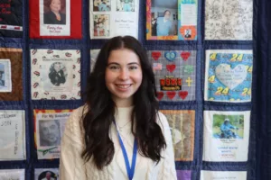 A young woman poses in front of a quilt.