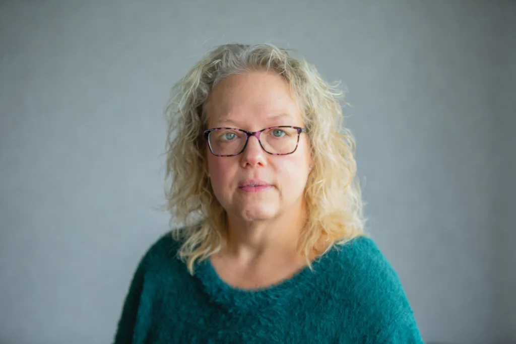 A woman poses for a photo in front of a background.