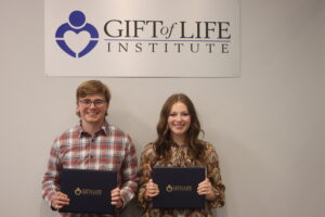 Two people - a man and woman - pose for a picture underneath a Gift of Life Institute sign.