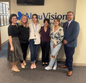 A group of men and women smiles for a photo in front of the AltruVision logo