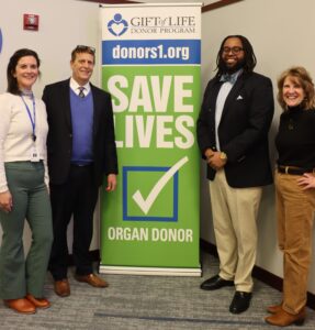 A group of men and women smile for a photo in front of an organ donor sign.