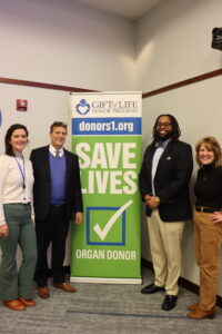 A group of men and women poses for a photo in front of a organ donor sign.