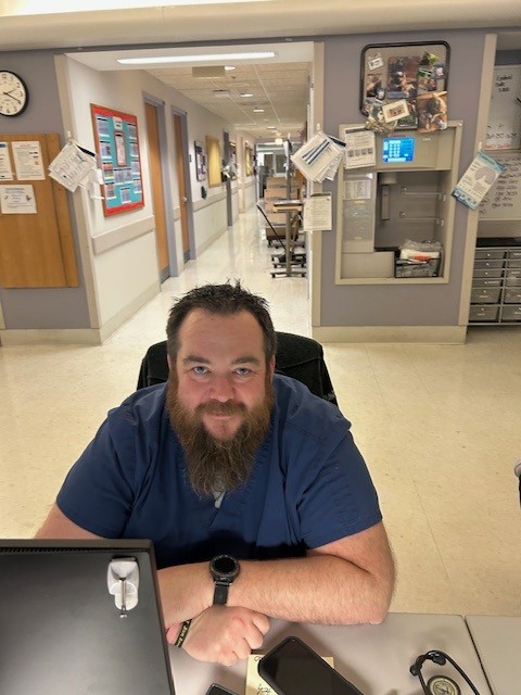 A nurse smiles for a photo while sitting at this desk in front of a computer monitor.