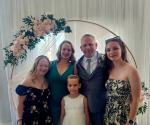A smiling family poses for a photo in front of a floral backdrop. 