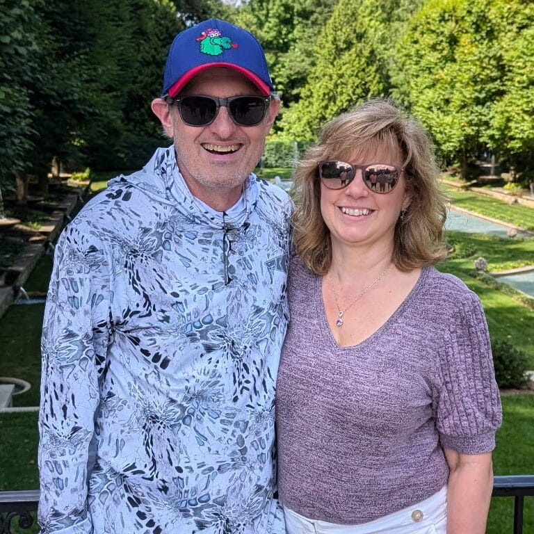 Tom smiles for a photo, accompanied by his wife.